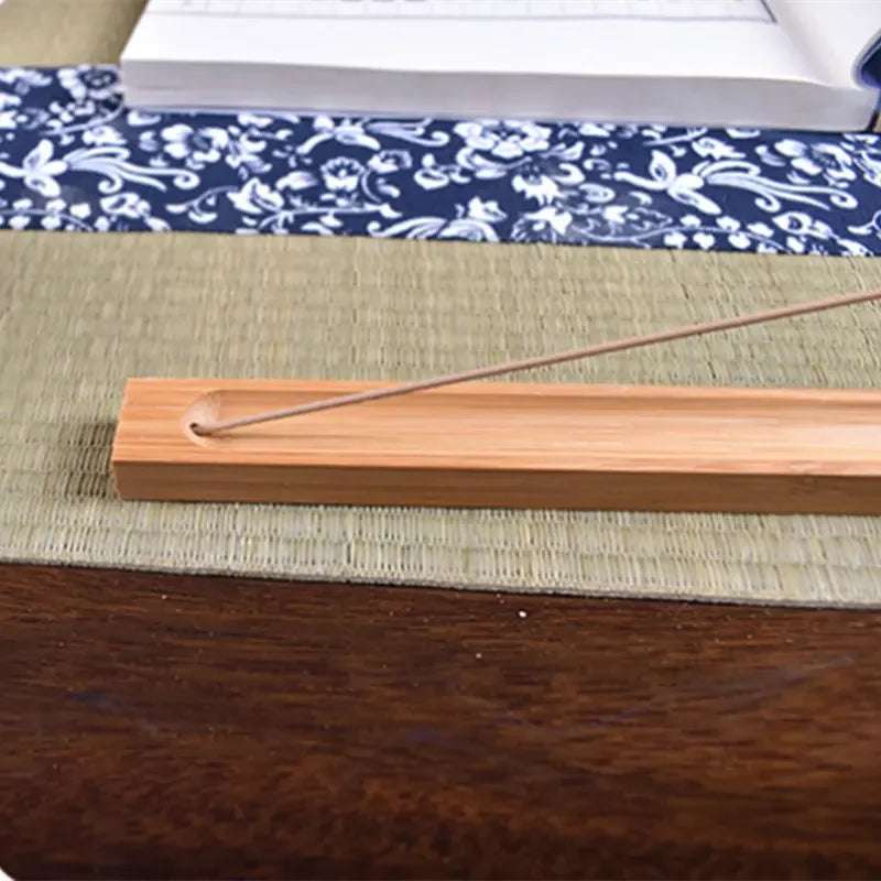 Wooden incense stick holder with an incense stick inserted, resting on a textured table surface.