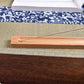 Wooden incense stick holder with incense stick resting in hole on decorative table setting.